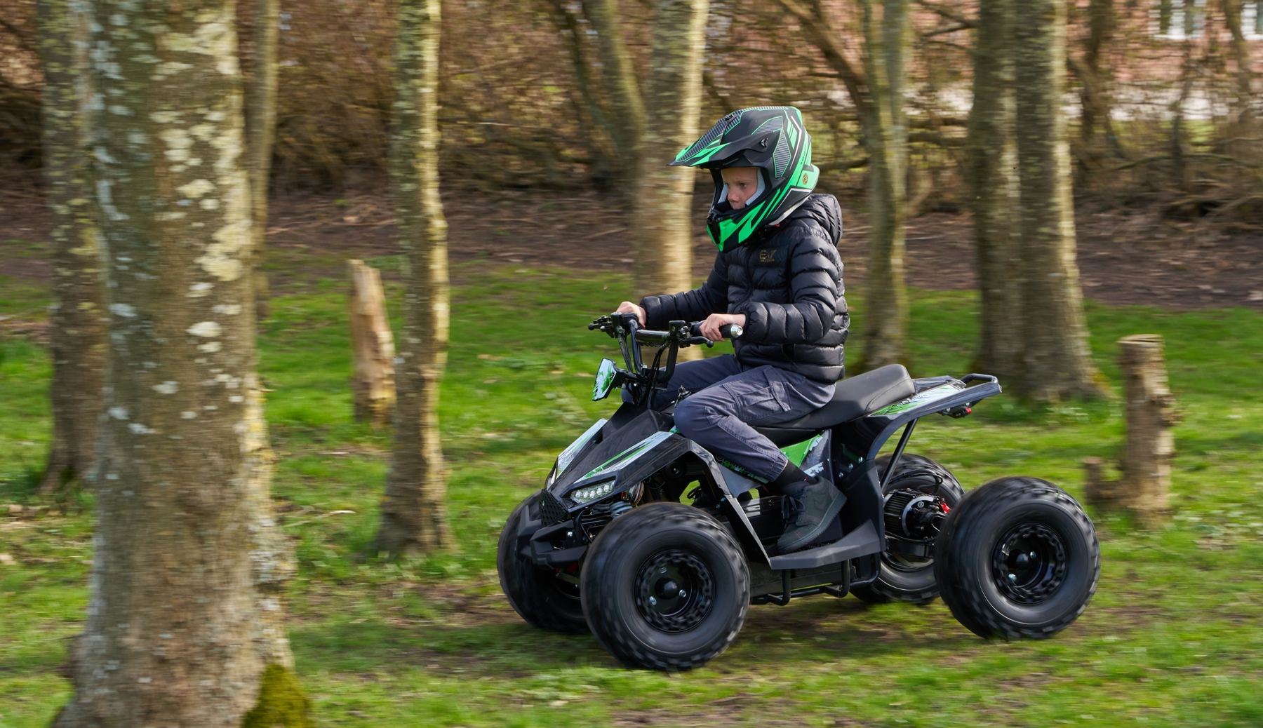 Dreng med grøn hjelm kører EL ATV mellem træerne